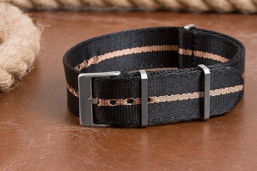 Crown and Buckle Supreme NATO strap in Black and Desert coiled on a leather surface