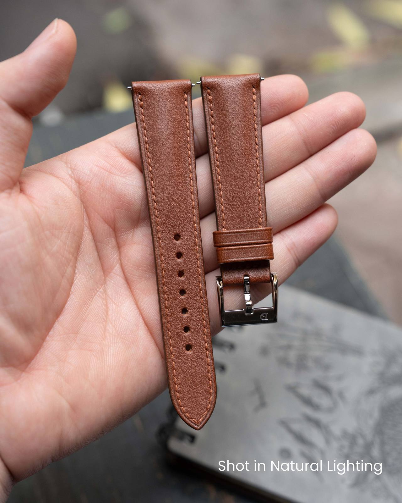 Delugs Signature strap in Fauve Baranil leather held in a hand, showing stitching and signed buckle