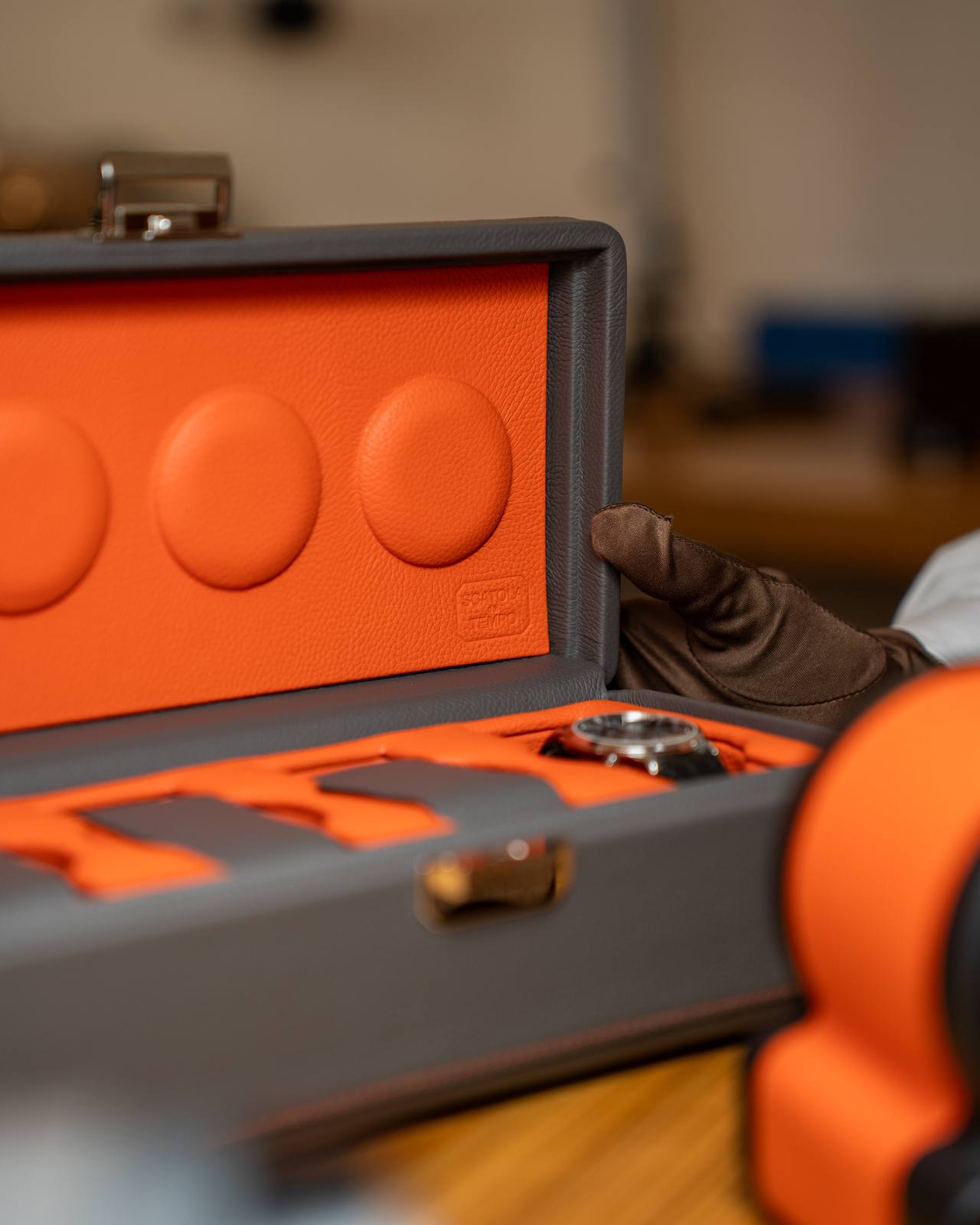 Gloved hand opening the Valigetta 4 to reveal its orange leather interior.